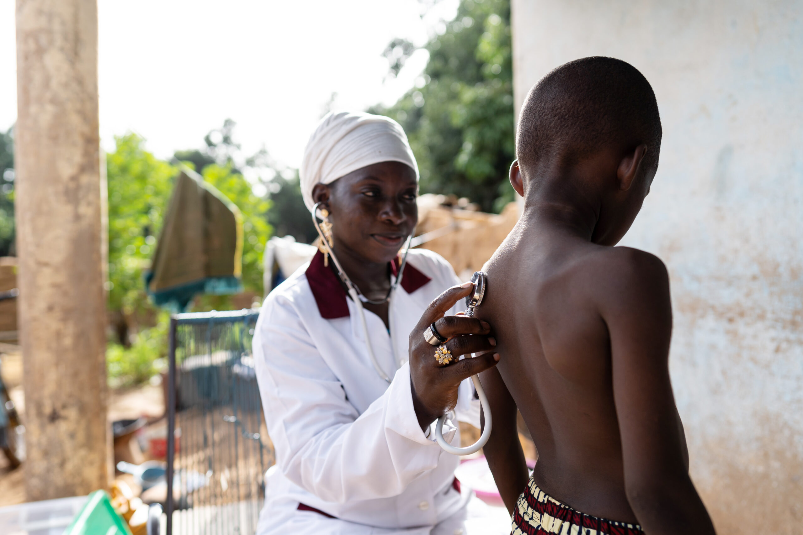In this image, a pediatrician is visiting an african village family to check the general health status of an ill black schoolboy with a suspected infectious disease